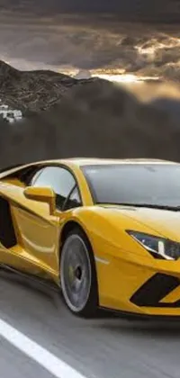 This phone live wallpaper showcases a vibrant yellow sports car driving along a winding mountain road