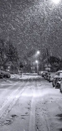 This phone live wallpaper showcases a beautiful black and white photograph of a suburban street at night during snowfall