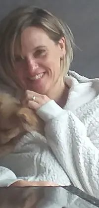 This charming phone live wallpaper showcases a woman tenderly holding a small dog, adorably wrapped in a cozy blanket