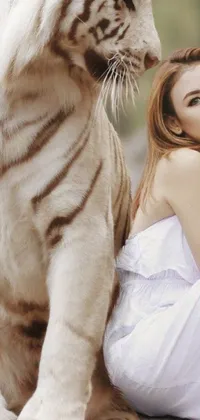 This live phone wallpaper features a stunning image of a white tiger sitting next to a woman on a rock