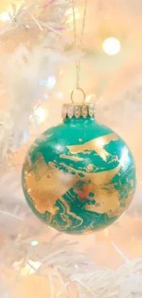 This Christmas-themed phone live wallpaper features a process art-inspired design of a close-up view of a stunning teal, white, and gold ornament hanging from a tree