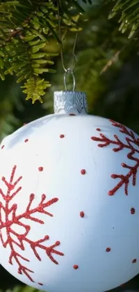 This phone live wallpaper features a close up of a Christmas ornament on a tree with a stippled design in white and red