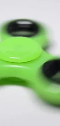 Looking for a playful and unique live wallpaper? Check out this green fidget spinner sitting on a white table with a kinetic art background! This design features spinning toys, shurikens and other fun objects in the air as the fidget spinner spins in real-time on your screen