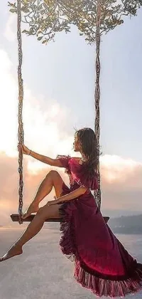 This phone live wallpaper features a gorgeous woman sitting on a swing in a floating position against a beautiful scenic background of a sunrise