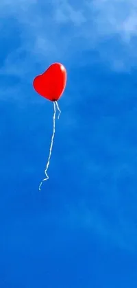This phone live wallpaper depicts a red balloon with a heart-shaped balloon trailing behind, flying in a bright blue sky