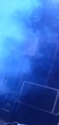 This live phone wallpaper showcases a captivating close-up image of a man holding a microphone on a stage, set amidst a blue smoke-filled environment captured on an iPhone