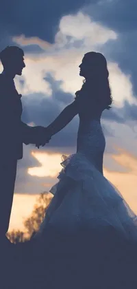 Looking for a romantic live wallpaper for your phone? Look no further than this stunning silhouette of a bride and groom holding hands against a picturesque sky