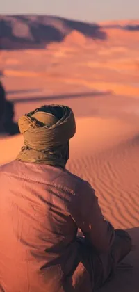 This phone live wallpaper showcases a man wearing traditional clothing and a turban, seated in the desert