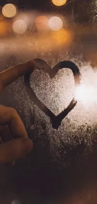 This live phone wallpaper artwork features a heart drawn on a frosted glass or a picture held by a person against a background of clouds and moon