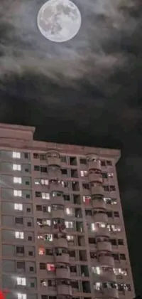 This live wallpaper depicts a majestic skyscraper illuminating the night sky while an enchanting full moon hovers above