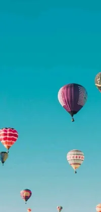 Transform your phone screen with this captivating live wallpaper featuring a fleet of vivid hot air balloons soaring across a scenic teal-colored sky