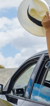 This phone live wallpaper features a triumphant woman sitting in a vintage car on a sunny day