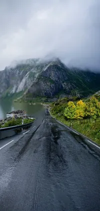 If you're looking for a stunning live wallpaper for your phone, you'll love this one! The wallpaper features a winding road beside a calm body of water, with rolling mountains in the distance