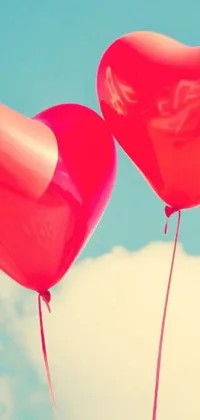Add a touch of whimsy and romance to your smartphone with this delightful live wallpaper! Two heart-shaped red balloons soar high against a clear blue sky, gently bouncing as they float