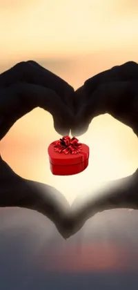 This live wallpaper for phone showcases a delightful and romantic image of a person holding a gift, while making a heart gesture with their hands