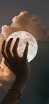 This phone live wallpaper features a surrealistic depiction of a person holding up a full moon in the night sky