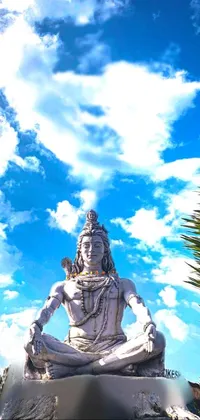 This live wallpaper showcases an awe-inspiring statue of a man sitting atop a rock against a backdrop of stunning blue clouds