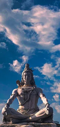 This phone live wallpaper boasts an intricately designed Samikshavad statue sitting atop a rock, surrounded by blue skies and clouds