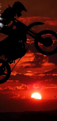 This live phone wallpaper showcases a stunning scene of a dirt bike rider soaring through the air against a breathtaking red sunset