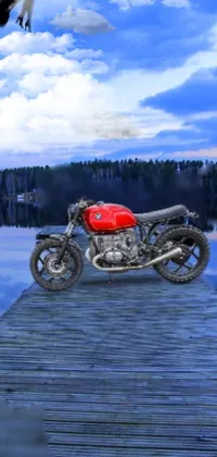 This phone live wallpaper depicts a vintage motorcycle with a demon theme, parked on a wooden dock next to a serene lake surrounded by lush trees