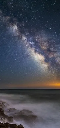 This mobile live wallpaper features an awe-inspiring view of the Milky Way galaxy shining brilliantly above the ocean