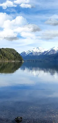 This phone live wallpaper depicts a serene water body surrounded by trees with the stunning backdrop of snow-capped mountains in Chile