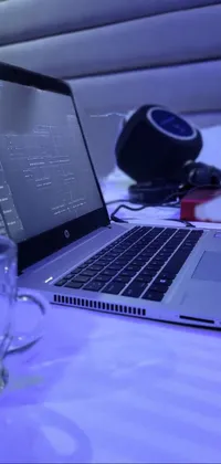 This live phone wallpaper features a laptop computer resting on a bed against a captivating backdrop, designed by a skilled artist