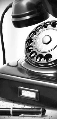 This phone live wallpaper features a vintage closeup photograph of an antique phone and pen resting on a desk
