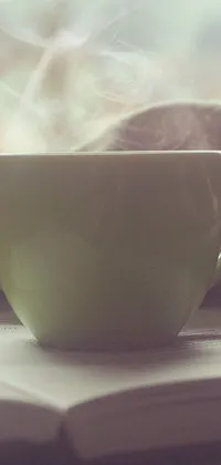 This live wallpaper for phone features a cup of coffee and a book set against a pale green backdrop, with a warm and cozy vibe to it