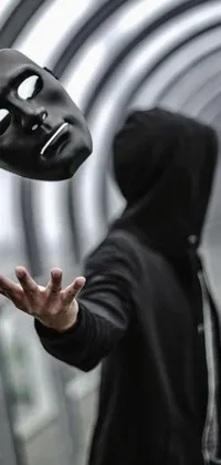 This live wallpaper depicts a figure in a black hoodie throwing a black mask into the air against a metallic blue and cybernetic face background