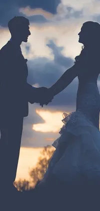 This stunning live wallpaper portrays a loving couple holding hands in silhouette at their wedding against a beautiful sunset sky