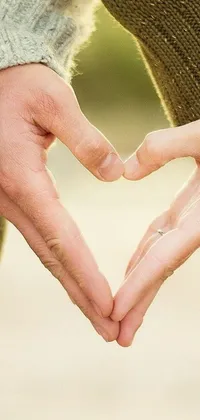 This phone live wallpaper features a heartwarming image of two people holding their hands to form a romantic heart shape