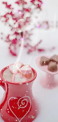 This live wallpaper depicts a cozy image of a cup of hot chocolate with marshmallows in it, against a romantic backdrop of pink and red colors