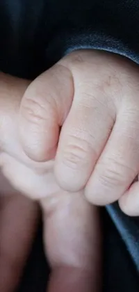 This phone live wallpaper depicts a heartwarming image of an individual's gnarled fingers holding a baby's hand