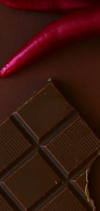 This live wallpaper showcases a luscious piece of chocolate nestled near a fiery chili, set upon a sleek modern table
