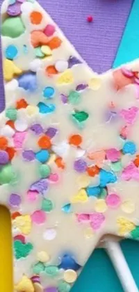 This live wallpaper features a close up of a star shaped cake on a stick, decorated with colorful confetti, solid colored shapes, and glitter sprinkles
