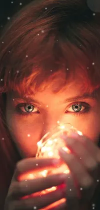 This phone wallpaper boasts a captivating portrait of a red-haired girl holding a bright light, surrounded by an abstract mix of glass and lights