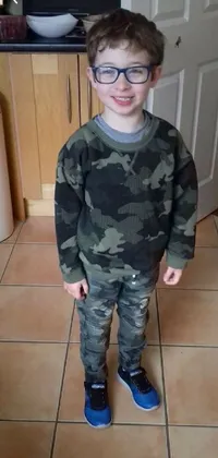 This live phone wallpaper features a young boy wearing glasses standing on a tiled floor wearing camo