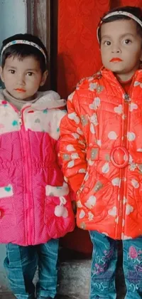 This playful phone live wallpaper showcases a vividly colored and patterned background of polka dots with a close-up photo of two young children wearing vibrant orange reflective puffy coats