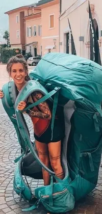 This phone live wallpaper displays a young woman with a huge backpack and a roof rack wearing a teal outfit, who appears joyful