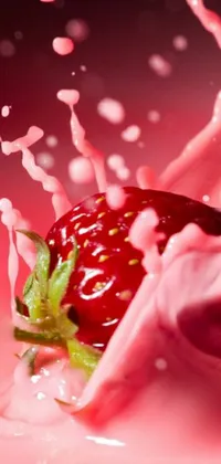 This phone live wallpaper features the stunning closeup of a ripe strawberry falling into a pale pink liquid