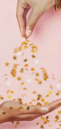 This live phone wallpaper features two hands holding sparkling gold stars on a soft pink background