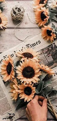 This phone live wallpaper features a bouquet of sunflowers and a newspaper, creating a cozy and aesthetic vibe