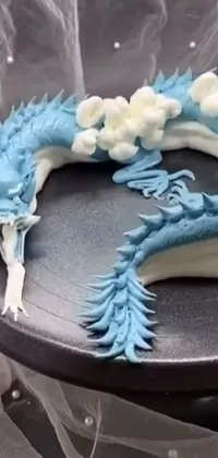This phone live wallpaper displays a gorgeous blue and white cake atop a black plate, with a fantasy-inspired background of a fire-breathing dragon