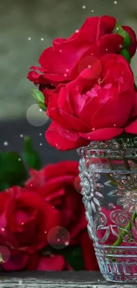Looking for a stunning live wallpaper for your phone? Look no further than this breathtaking image of a vase full of bright red roses! The flowers are arranged in a glass vase and the whole image is set on a wooden table, creating a beautiful and stylish effect