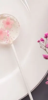 This phone live wallpaper features a whimsical design with colorful lollipops on a white plate surrounded by sakura flowers