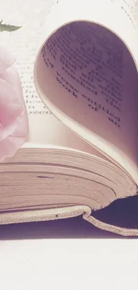 Immerse yourself in the vintage charm of this phone live wallpaper featuring a delicate pink rose resting on an open book