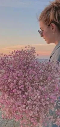Are you searching for a phone live wallpaper that is both captivating and aesthetically pleasing? Look no further than this stunning image of a woman standing on a beach holding a bunch of gypsophila flowers and a photo