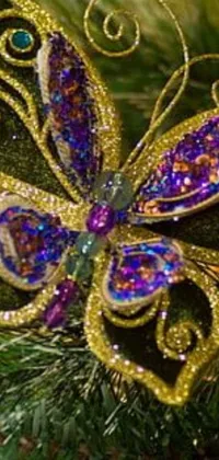 This phone live wallpaper features a stunning butterfly ornament adorning a glowing Christmas tree, with gold, green, blue, and purple hues creating a vibrant backdrop