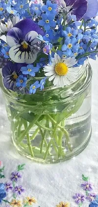 This phone live wallpaper features an animated close up of a jar of colorful flowers on a wooden table, complete with butterfly embroidery, morning dew and bright white daisies
